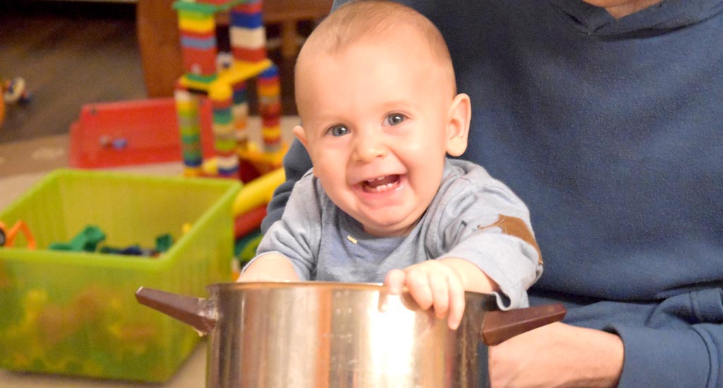 Baby spielt mit Kochtopf und kleckert: Symbolbild für spielerisch Essen lernen